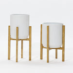 Two modern metal plant pots with ribbed designs stand elegantly against a plain background, each perched on wooden stands.
