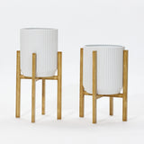 Two modern metal plant pots with ribbed designs stand elegantly against a plain background, each perched on wooden stands.