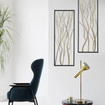 A modern living space featuring a dark blue armchair, a gold desk lamp on a round table, a potted plant, and striking modern wall art that serves as a focal point with its gold and silver branch designs.
