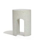 A white, cylindrical stool with a speckled pattern and a U-shaped cutout at the bottom sits elegantly against a plain background, perfect as an outdoor side table crafted from ivory white cement.