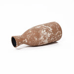 A rustic, textured, brown ceramic bottle lies on its side against a plain white background, exuding the handcrafted earthenware charm of traditional artisanship.