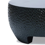 Close-up of a black cement outdoor coffee table, featuring a modern, hammered surface design with a textured, rounded finish.
