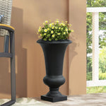 A weather-resistant black urn planter with yellow flowers sits on a porch beside a chair with a woven seat and backrest.