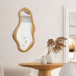 A wooden mirror with an irregular shape and a pine frame hangs on a white wall, infusing the space with natural energy. Nearby, a round wooden table adorned with vases and dried plants enhances the organic decor.