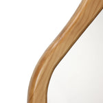 A close-up view of a mirror with a wooden frame, showcasing smooth curves and an organic wood grain texture, it serves as a versatile accent to any space.