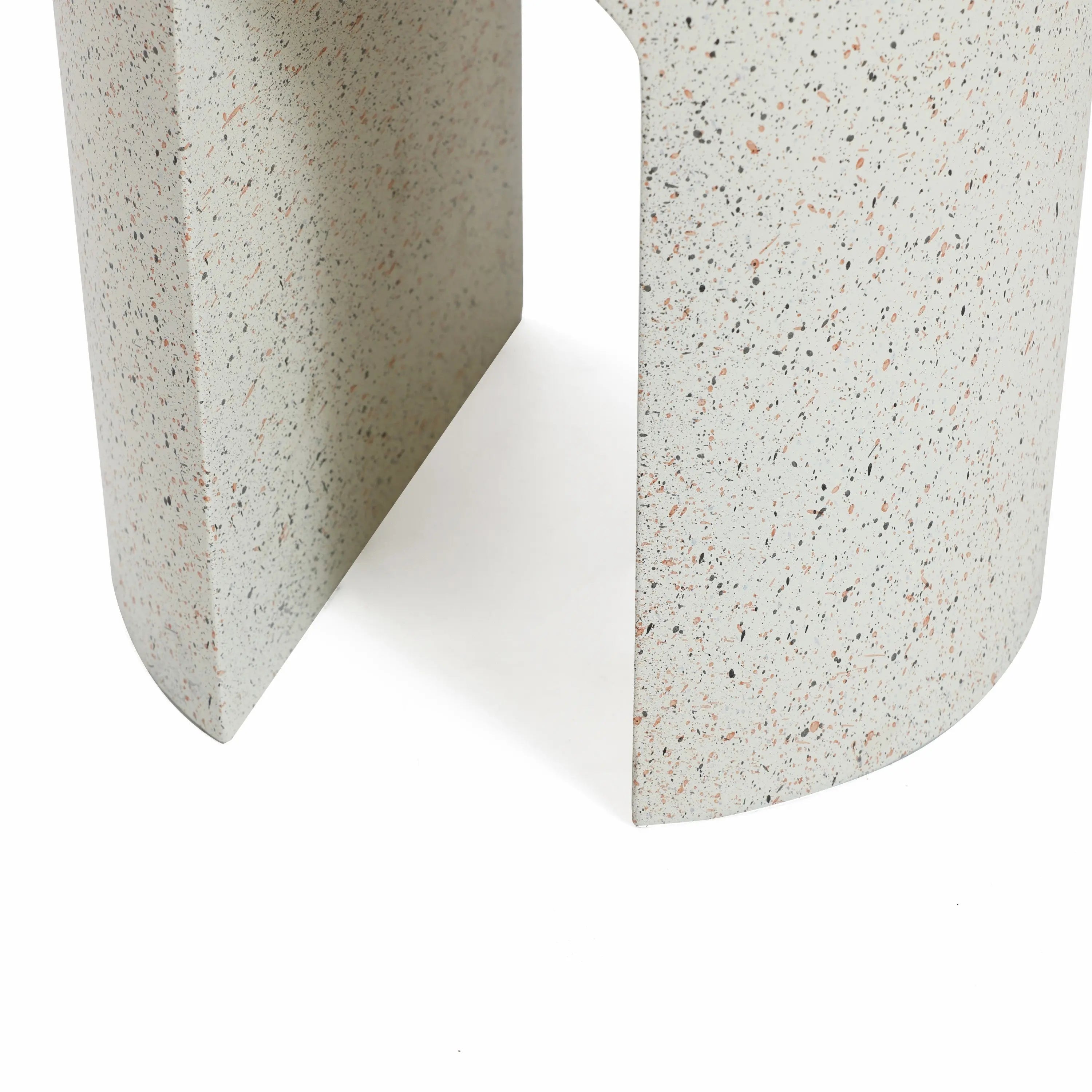 Close-up of a textured, speckled light gray surface with an ivory-white cement finish, featuring a geometric opening that suggests a modern sculpture or architectural detail—an ideal touch for an outdoor side table.