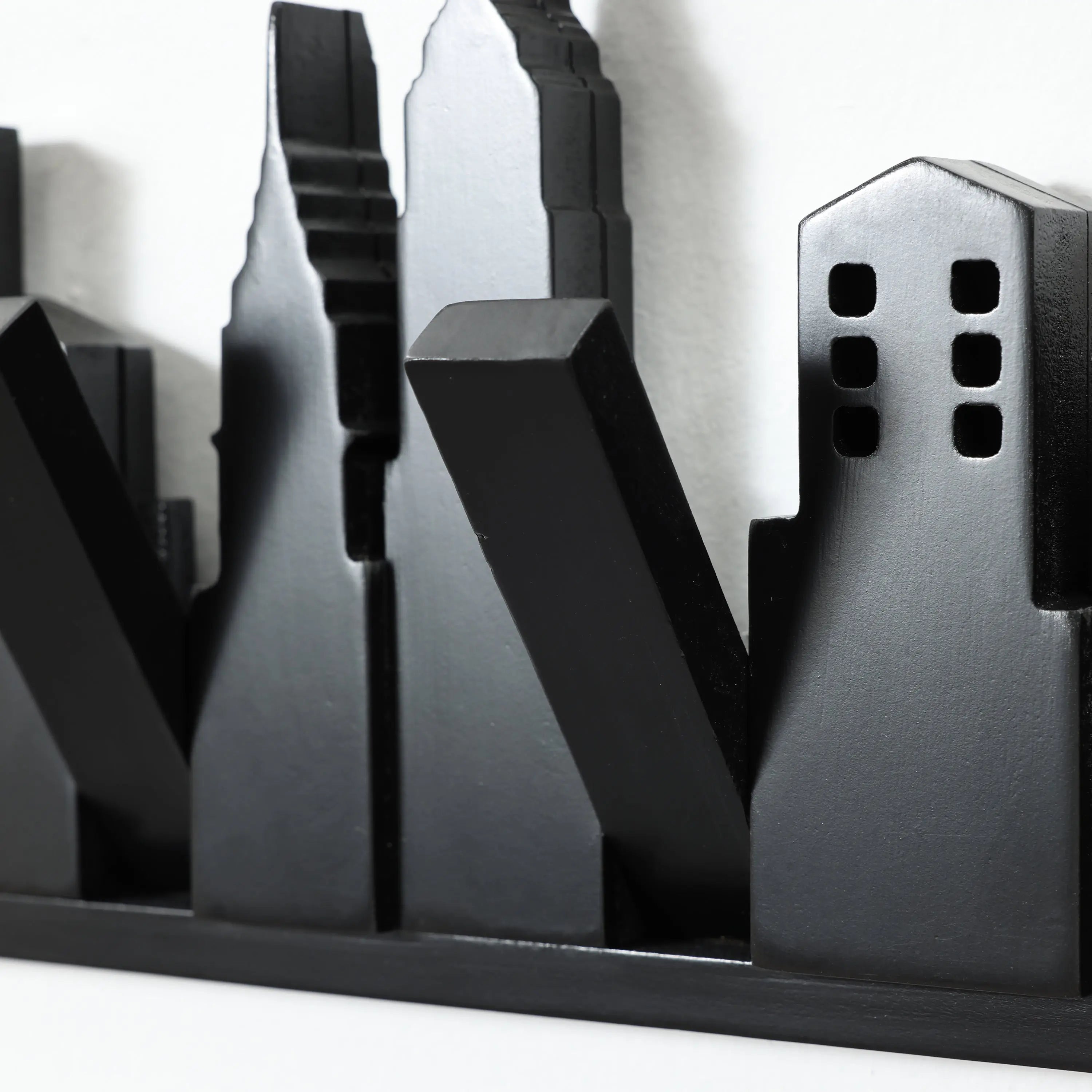 A metallic black sculpture depicting a stylized city skyline with various building shapes against a white background cleverly doubles as a wall-mounted coat rack, featuring discreet flip-down hooks to blend artistry and functionality seamlessly.