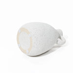 A vintage vase in white-speckled ceramic lies on its side, revealing a round base with four small rubber pads—an exquisite piece for any home decor setting.