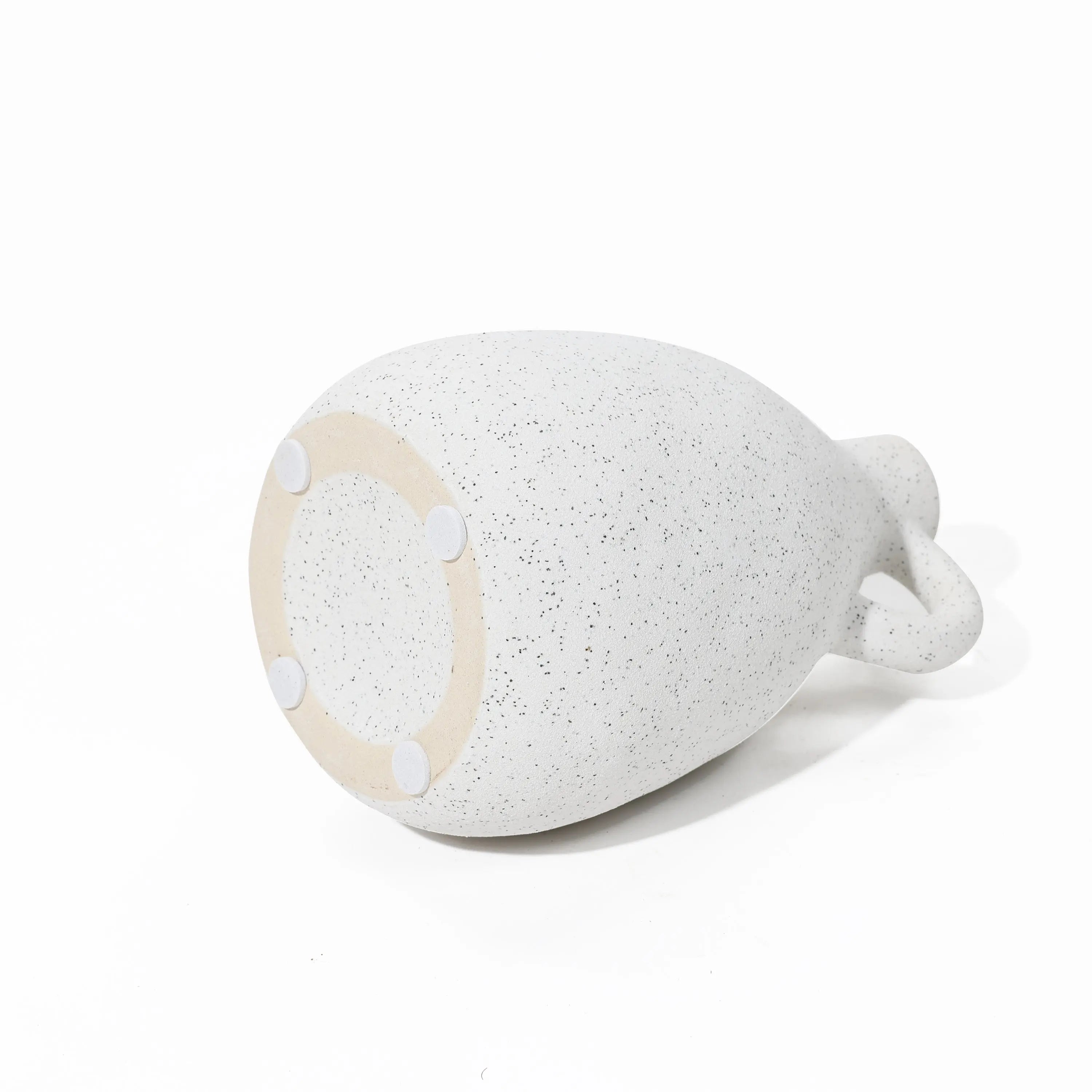 A vintage vase in white-speckled ceramic lies on its side, revealing a round base with four small rubber pads—an exquisite piece for any home decor setting.