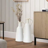 Two white ceramic vases with dried branches stand on a wooden floor next to a light wood cabinet in a room with vertical striped walls, embodying modern minimalist design. This harmonious home decor element is perfect for those who appreciate subtle elegance.