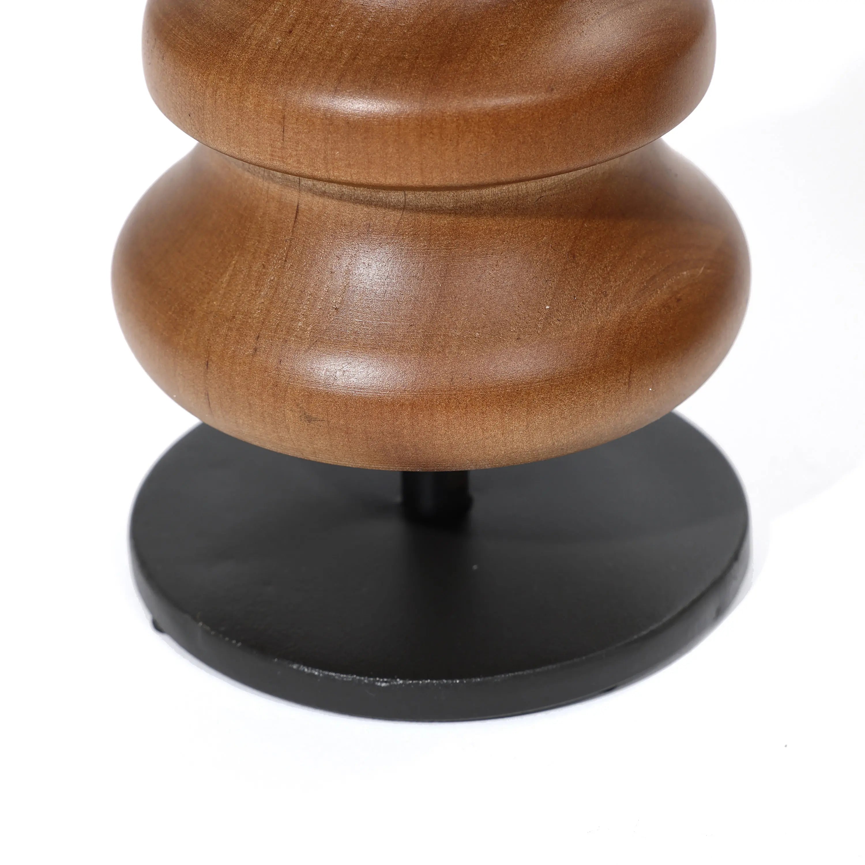 A close-up reveals a wooden object crafted from birch, showcasing smooth, curved shapes on a round, black base against a white background. This elegant piece doubles as a striking candle holder and effortlessly enhances any home decor setting.