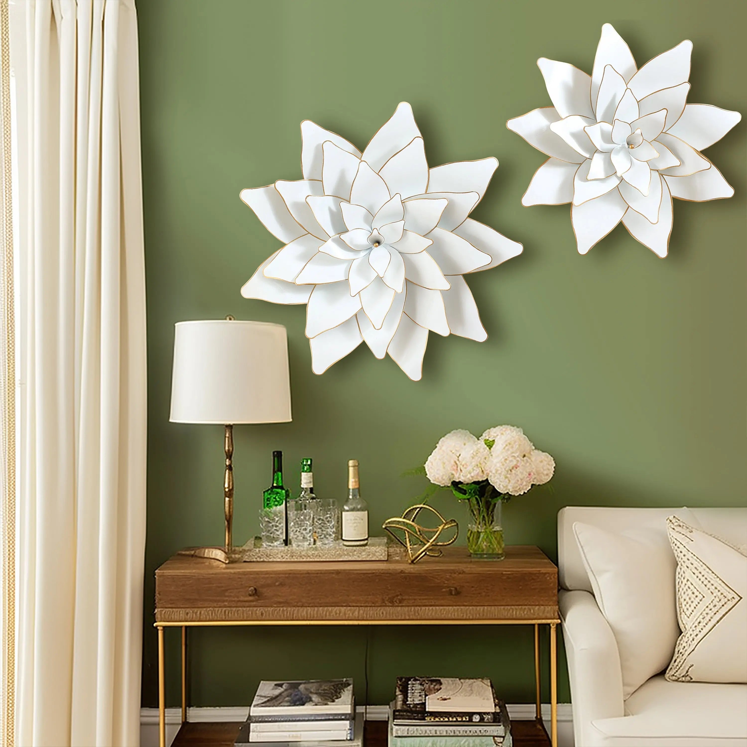 The room features green walls adorned with white lotus wall decorations, a wooden table, bottles, and a lamp. A bouquet of flowers graces the space alongside a white couch and an array of books, creating an inviting ambiance.
