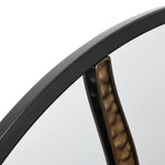 Close-up of a round wall mirror with a black frame and an artistic design featuring a decorative metallic accent inside.