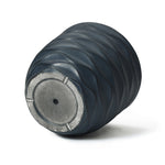 A dark, ribbed, cylindrical pot planter with a flat circular base and a central hole, crafted from durable magnesium oxide.