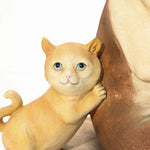A small, golden cat figurine with blue eyes leans against a larger beige French bulldog statue on a wooden surface, adding an eclectic style to the decor.