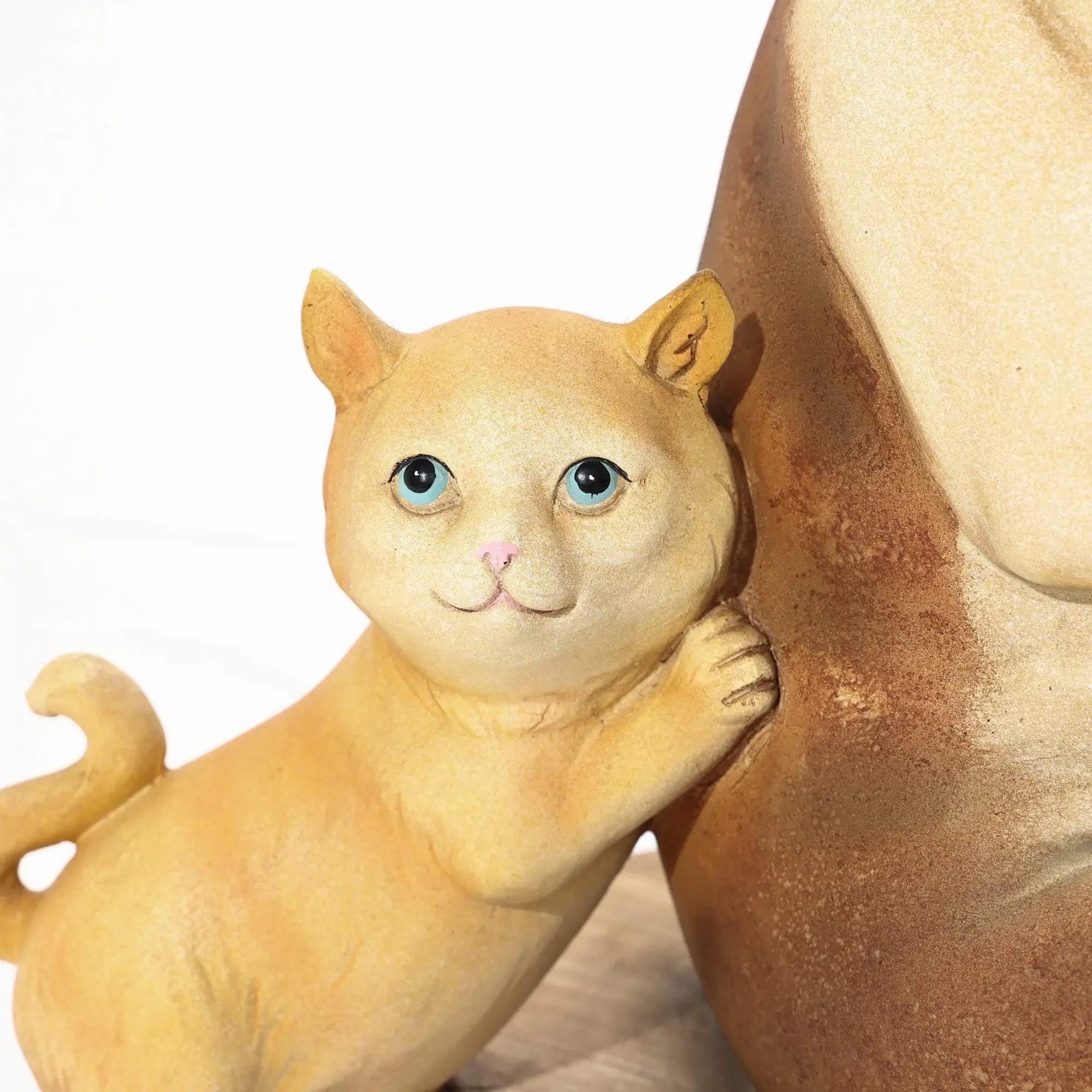 A small, golden cat figurine with blue eyes leans against a larger beige French bulldog statue on a wooden surface, adding an eclectic style to the decor.