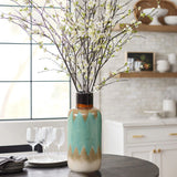 A coastal-inspired vase with a zigzag pattern holds white flowering branches on a table set with four wine glasses in a kitchen.