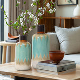 Two turquoise vases exude nautical charm with blooming branches on a wooden table beside a brown bowl and stacked books in a modern living room.