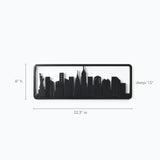 A black silhouette of a city skyline adorns this wall-mounted coat rack, framed in solid fir wood. Its dimensions are 22.3 wide, 8 high, and 1.5 deep, featuring cleverly designed flip-down hooks for hanging convenience without compromising style.