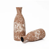 Two textured brown ceramic vases with white speckles, exuding rustic charm, sit against a white background. One stands upright while the other lies on its side, showcasing the beauty of handcrafted earthenware.