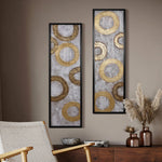 Two rectangular artworks with gold metal designs hang on a wall above a wooden cabinet, next to a woven chair and decorative vases filled with pampas grass, creating stunning wall decor that elevates your home decor.