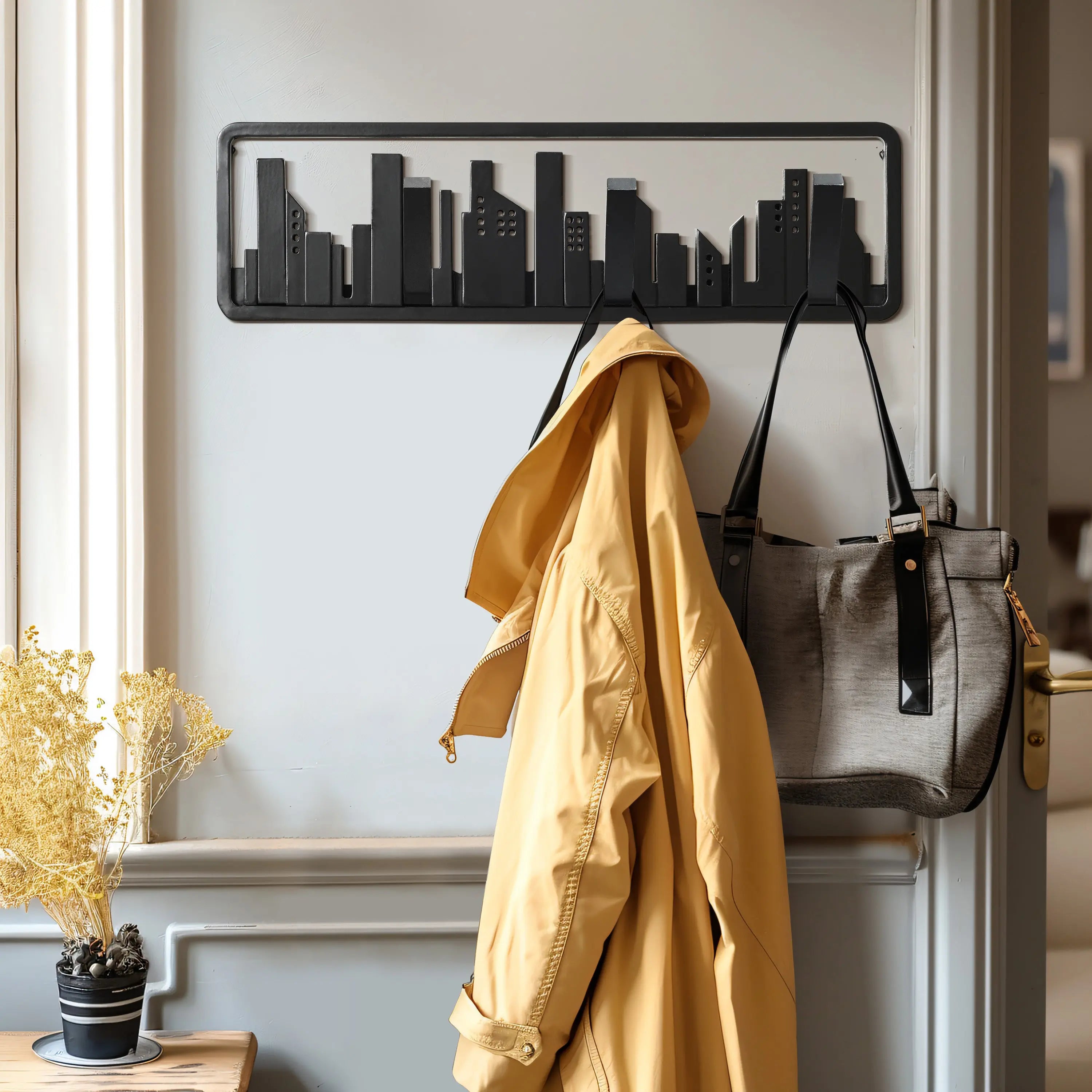 A coat and bag hang on a wall-mounted rack crafted from solid fir wood, its sleek design mimicking a city skyline. Flip-down hooks add functionality, while a nearby potted plant brings a touch of nature to the urban-inspired decor.