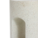 Close-up of a speckled, rounded outdoor side table with a U-shaped design, featuring a curved indentation and showcasing its textured ivory white cement surface.