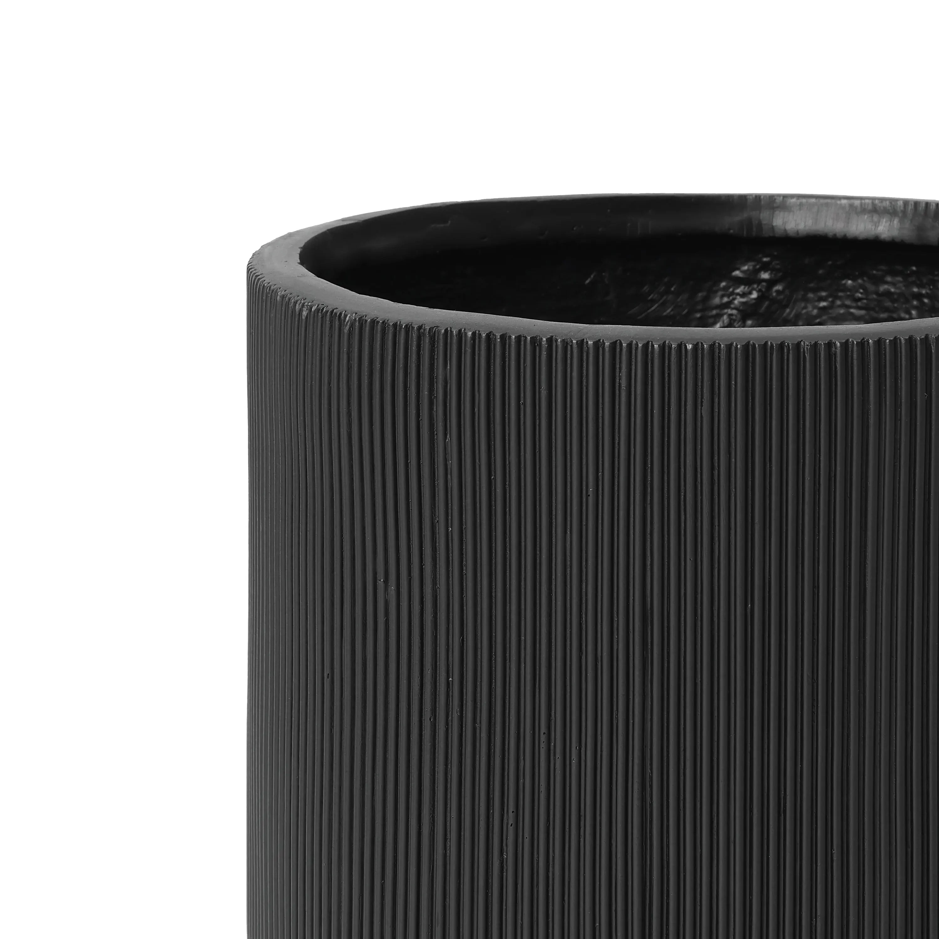 Close-up of the upper half of a black, ribbed cylindrical vase, crafted from magnesium oxide material, featuring a smooth interior.
