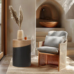 A stylish living room corner showcases a cushioned wicker chair alongside a versatile piece: a modern round side table with a wooden top. A vase with pampas grass complements the warm-toned interior, complete with a built-in shelf and lamp in the background.