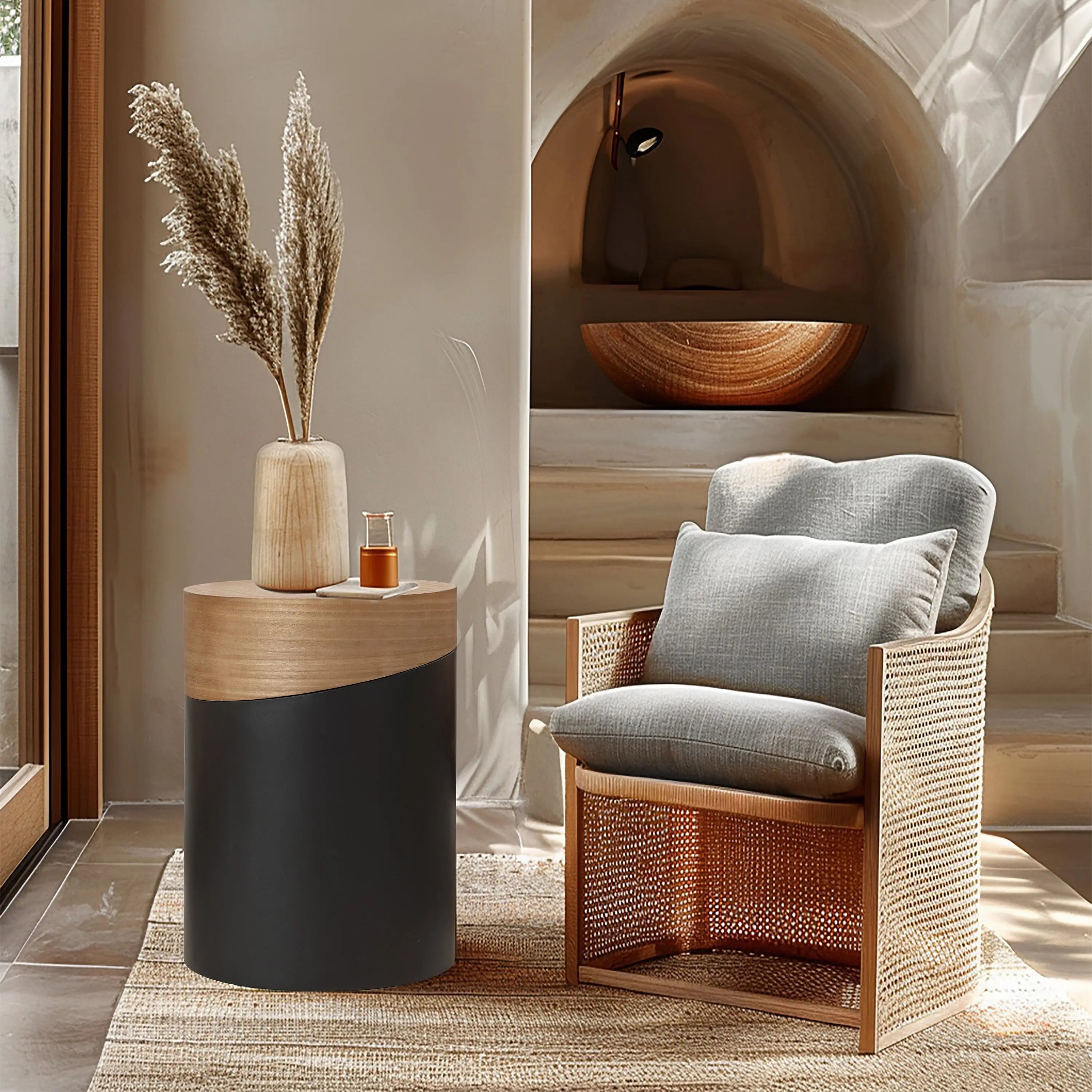A stylish living room corner showcases a cushioned wicker chair alongside a versatile piece: a modern round side table with a wooden top. A vase with pampas grass complements the warm-toned interior, complete with a built-in shelf and lamp in the background.