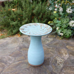 ceramic bird bath in backyard with tropical plants in background
