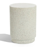 A textured, cylindrical, light-speckled concrete pedestal with vertical ridges stands on a flat surface, casting a shadow. This versatile table effortlessly blends function and style, offering an elegant touch to any space.
