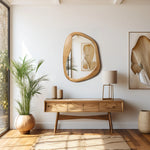A modern, minimalist room showcases organic decor with a wooden console table adorned with vases, a mirror, framed artwork, and a floor plant. A natural ambiance fills the space as light streams in through a large window, highlighting the table lamps subtle glow.