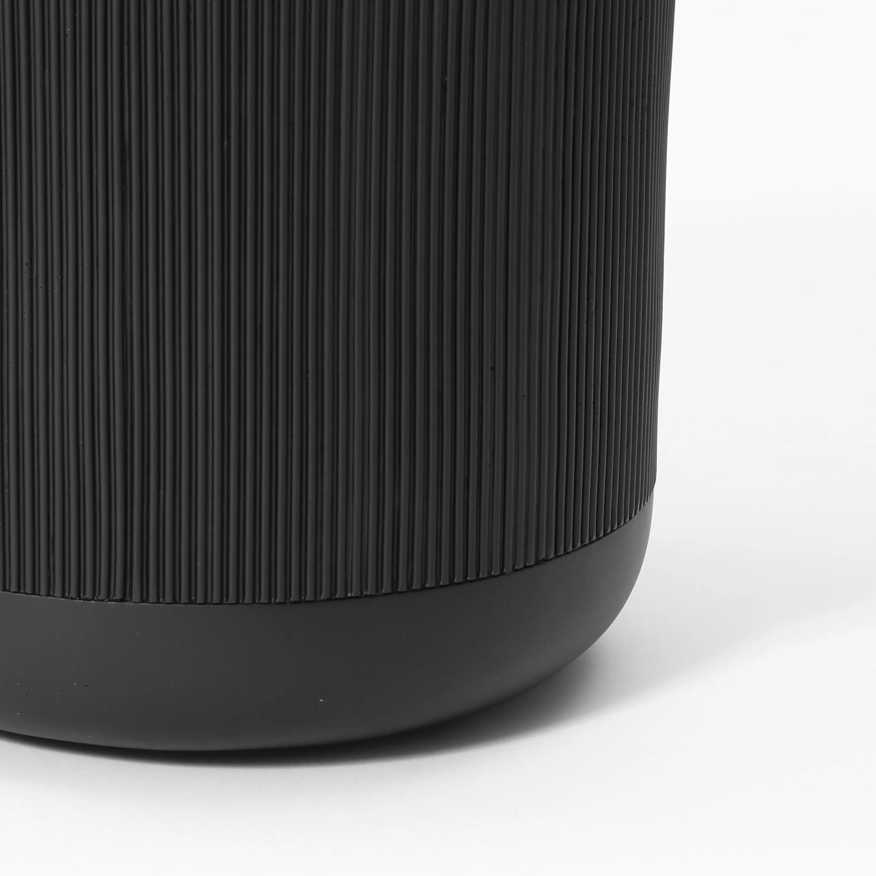 Close-up of a black cylindrical object with vertical ridges and a smooth base, resembling the sleek design of a stripes pattern planter, on a white background.