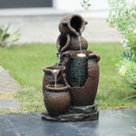 A rustic urn outdoor fountain with three tiered urns pours water in succession, set on a stone base and illuminated by an LED light—perfect garden decor for your tiled patio, surrounded by grass and plants.